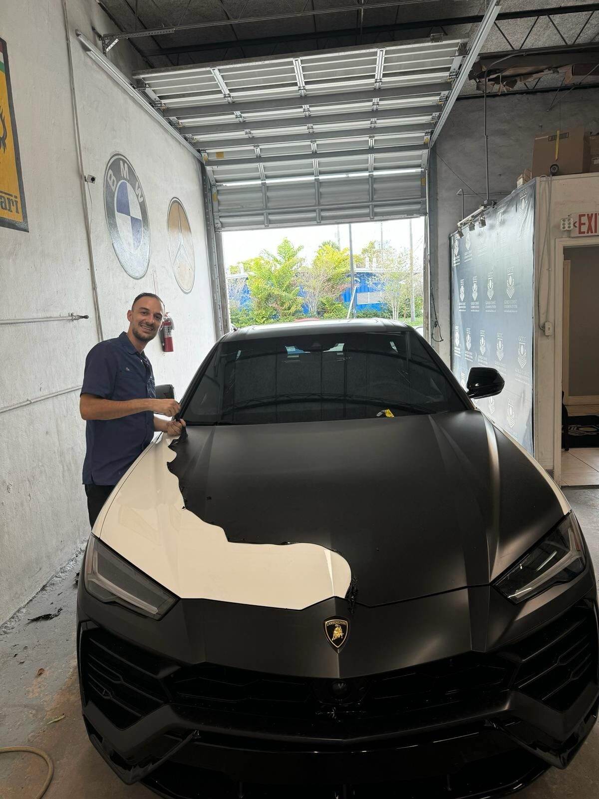 Technician working on a matte-black Lamborghini Urus at Gold Coast Collision Center