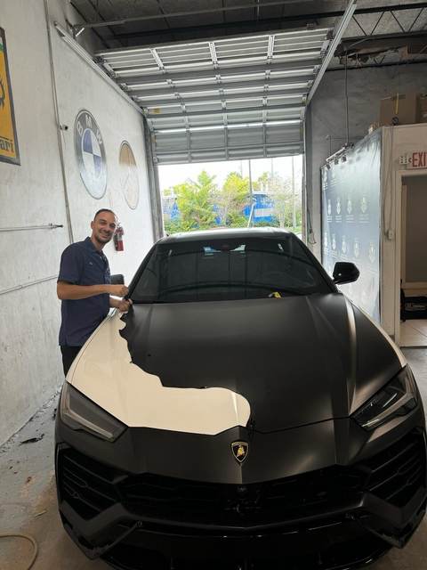 Technician working on a matte-black Lamborghini Urus at Gold Coast Collision Center