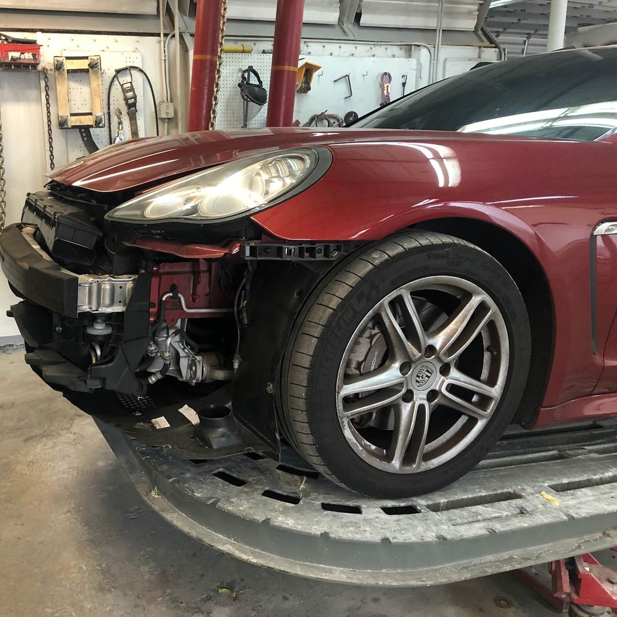 Red Porsche Panamera with the front end torn down for collision repair at Gold Coast Collision Center in Pompano Beach